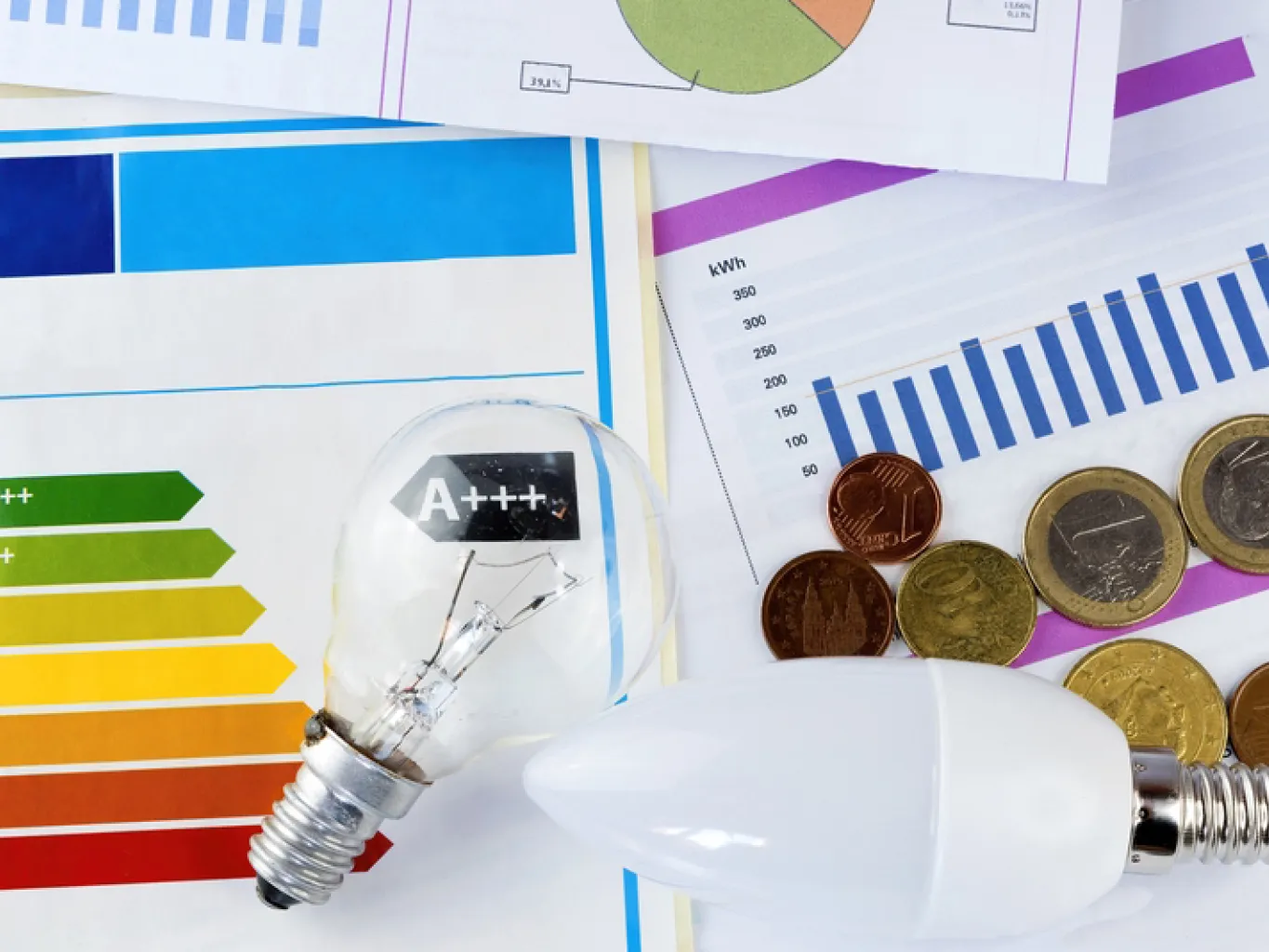 Dettaglio di etichette energetiche, bollette, lampadine e monete sparse su un ripiano